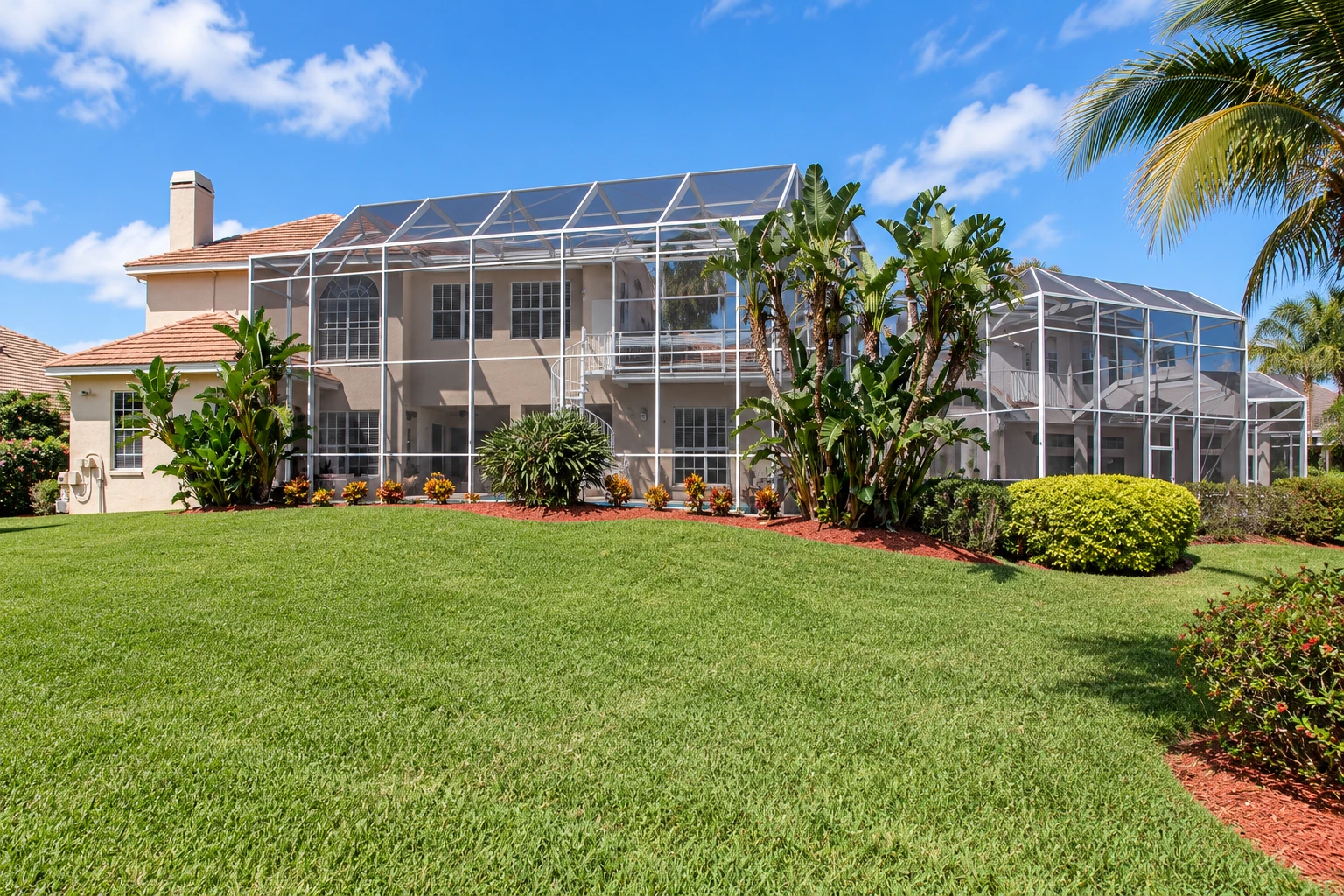 A large screened patio enclosure spans the back of a two-story home, opening onto a broad green lawn and tropical landscaping.