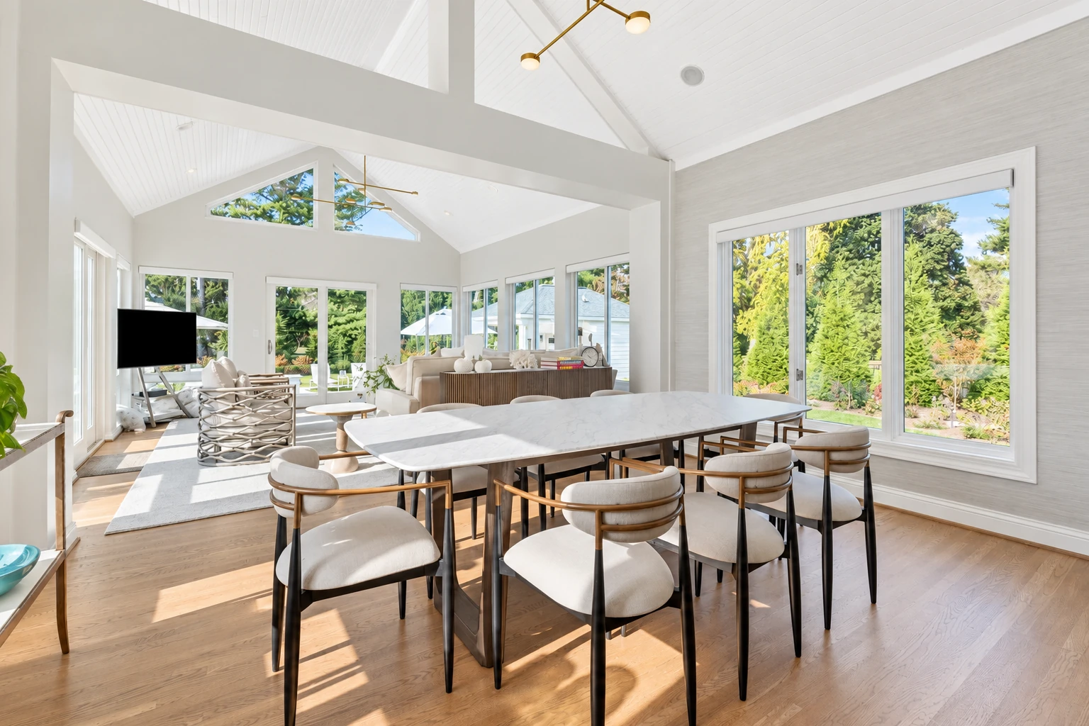Spacious vinyl sunroom with white framing, large windows, a dining table, and an adjacent living area.